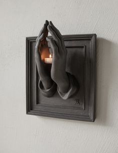 a light that is on the side of a wall with hands holding something in front of it