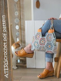 a woman sitting on a stool holding a purse next to a small white and brown dog