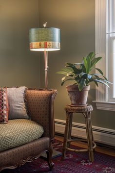 a living room with a chair, lamp and potted plant on the floor in front of a window