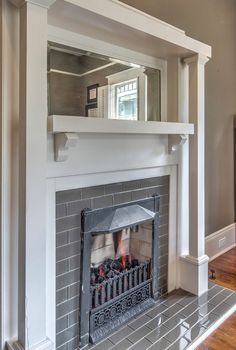 a fireplace with a mirror above it in a room that has wood floors and gray walls