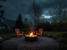 two chairs sitting around a fire pit in the middle of a yard at night time