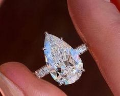 a close up of a person holding a ring with a pear shaped diamond on it