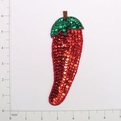 a sequinized red chili pepper ornament with a green leaf on it