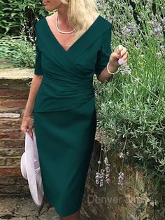 a woman in a green dress standing next to some bushes and lavenders with her hand on her hip