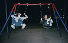 two people sitting on swings at night in the park, one holding onto another person's head