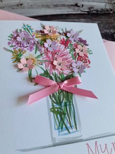 a bouquet of flowers in a vase with pink ribbon tied around the bottom and on top of a card