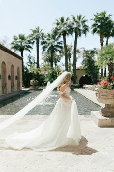 a woman in a wedding dress and veil is standing near a pool with palm trees