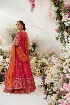 a woman standing in front of flowers wearing an orange and pink lehenga