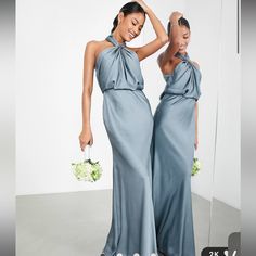 two women in long dresses standing next to each other and one is holding a bouquet