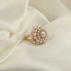 Life is movement! Building on this truth we worked on the concept of movement. This elegant cocktail ring handcrafted in gold holds a diamond pierced pearl dearly in the centre lined with prong-set diamonds, finished with an arrangement of pearls that move with you. Gold(14K) : 7.40g Brilliant cut Diamonds : (VS clarit Elegant White Crystal Proposal Ring, Elegant Cluster Rings For Proposal, Elegant Cluster Proposal Ring, Diamond Pearl Ring With Halo For Wedding, Dazzling White 14k Gold Cluster Ring, Diamond Halo Pearl Ring For Wedding, 14k Gold Pearl Ring With Center Stone For Wedding, Wedding Pearl Ring With Diamond Halo, White Cluster Rings With Rose Cut Diamonds