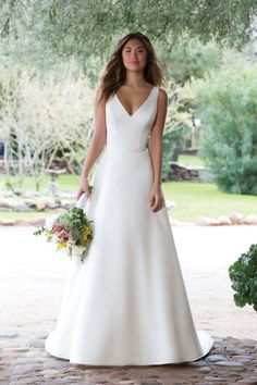 a woman in a white wedding dress standing under a tree with her hands on her hips