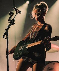 a woman standing next to a microphone while holding a guitar in front of a microphone