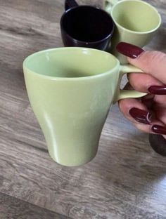 the woman is holding two coffee mugs on the table with her nails painted red