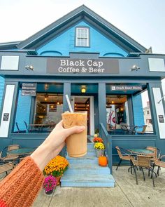 a hand holding a drink in front of a blue building with flowers on the steps