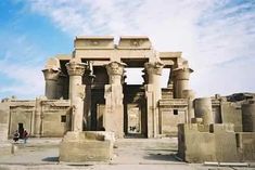 an ancient building with columns and people walking around it in the middle of desert area