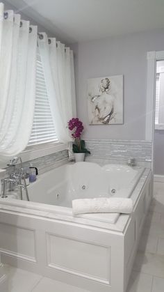 a white bath tub sitting in a bathroom next to a window with curtains on it