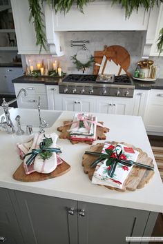 christmas presents are wrapped in paper and tied with ribbon on the kitchen counter top, surrounded by greenery