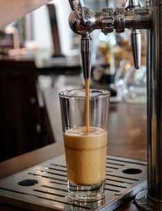 an espresso being poured into a glass on top of a coffee machine in a bar