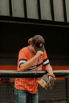 a baseball player leaning on the fence with his catcher's mitt in hand