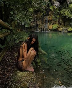 a woman sitting on the ground next to a body of water with fish in it