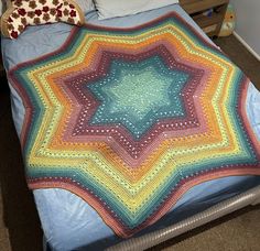 a crocheted blanket sitting on top of a bed next to pillows and blankets