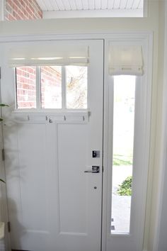 a white door with two windows and a plant in the corner on the right side