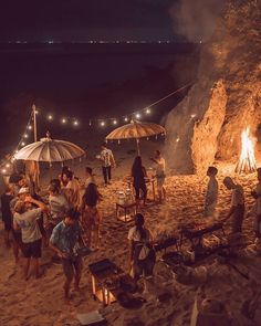 a group of people standing on top of a sandy beach next to an open fire