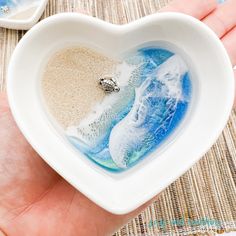 someone is holding a heart shaped bowl with sand in it