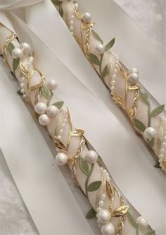 two pieces of ribbon with pearls and leaves on them, one is white and the other is gold