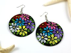 a pair of earrings with colorful flowers painted on them next to a starfish shell