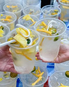 two people holding up cups filled with drinks and veggies on top of plastic containers