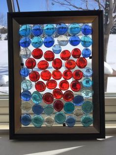 a framed glass window with red, white and blue circles on it in front of snow covered trees