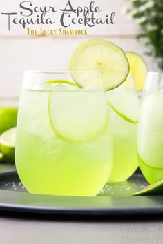 two glasses filled with lemonade and limes on a plate next to some flowers