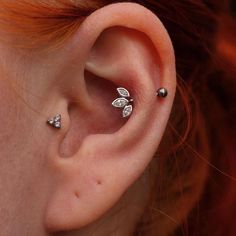 a woman with red hair is wearing three ear piercings on her left side, and two silver leaves are in the middle