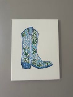 an embroidered cowboy boot is displayed on a white canvas with blue and green flowers in the center