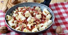 a pan filled with pasta and nuts on top of a checkered table cloth next to walnuts