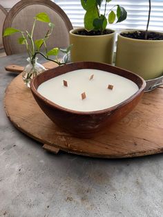 a wooden bowl filled with a candle on top of a table next to potted plants