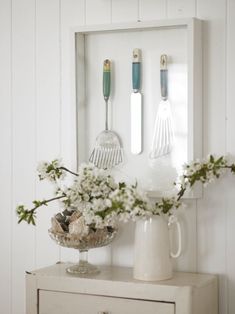 a white vase with flowers and utensils in it sitting on a table next to a mirror