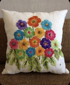 a white pillow with colorful flowers on it sitting on a brown couch next to a wall