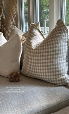 three pillows sitting on top of a couch in front of a window with large windows