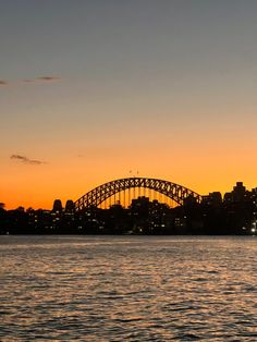 the sun sets over sydney, australia as seen from across the water with a bridge in the background