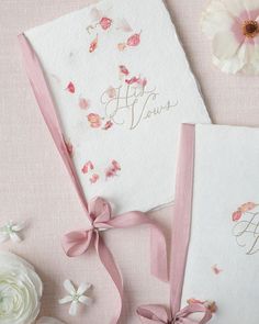 two wedding cards with pink ribbons and flowers on the table next to eachother