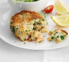 a white plate topped with crab cakes next to a bowl of salad and lemon wedges