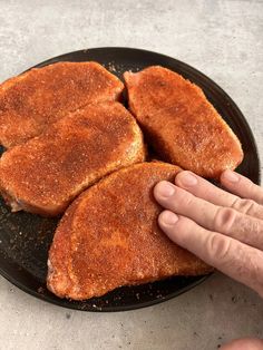 three pieces of fried meat on a black plate with a hand reaching for one piece