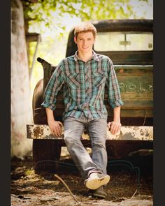 a young man sitting on the back of an old pickup truck posing for a photo