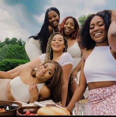 a group of women sitting on top of a picnic table with food and drinks in front of them