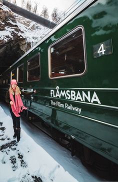 a woman standing next to a green train in the snow