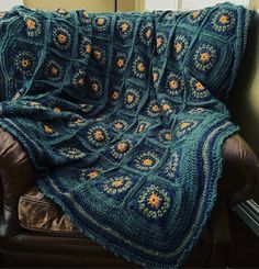 a blue crocheted blanket sitting on top of a brown leather chair next to a window