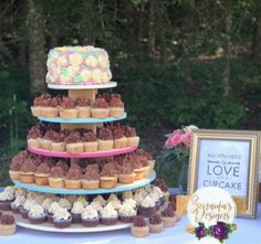 a three tiered cake with cupcakes on it and a sign that says love is in the background