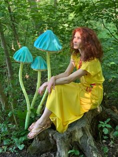 a woman sitting on top of a tree stump in the woods next to three blue mushrooms